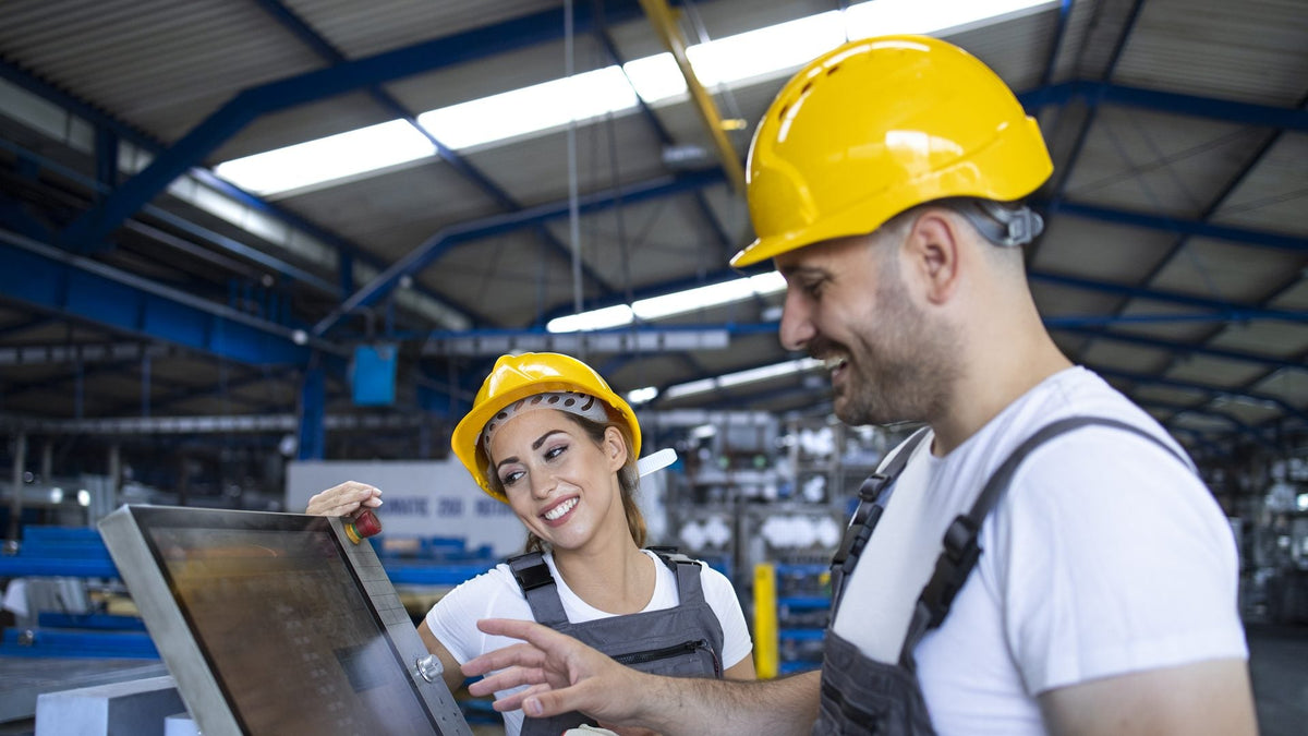 Operador experimentado enseña a una compañera a usar el panel táctil de una máquina industrial