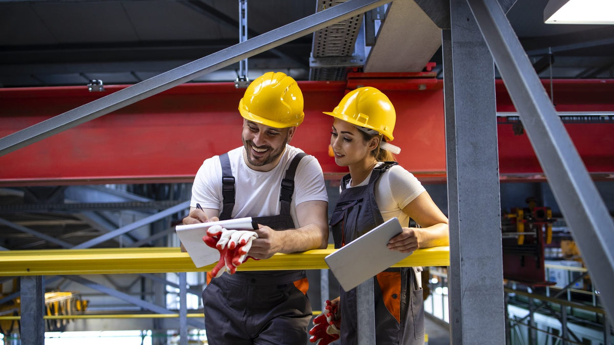 Dos trabajadores de planta con casco revisan el plan del turno en tabletas