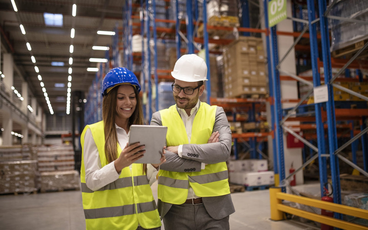 Una gerente y un supervisor revisan el inventario disponible en una tableta dentro de un centro de distribución